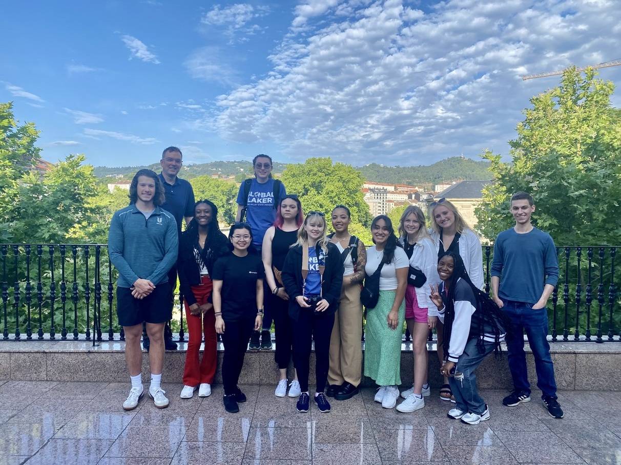 A group of students posing for a photo in Spain in front of a black railing with a beautiful scenic overlook